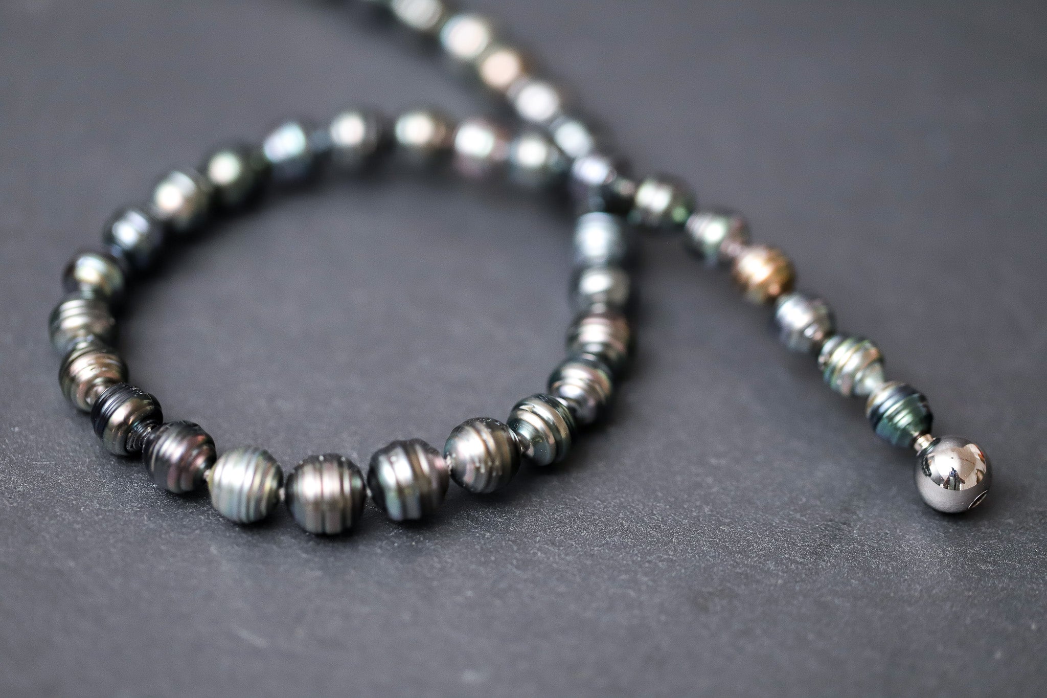 Dunkelgrün-graues Tahitiperlen-Collier mit gerillten Perlen und Wechselschließe aus Stahl.