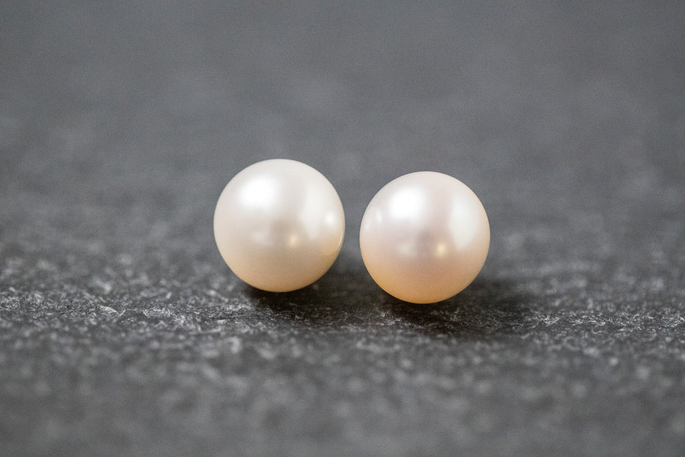 Zwei runde, weiße Frischwasserperlen mit glatter Oberfläche und zartem Glanz, nebeneinander liegend auf neutralem Hintergrund.