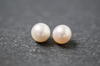 Zwei runde, weiße Frischwasserperlen mit glatter Oberfläche und zartem Glanz, nebeneinander liegend auf neutralem Hintergrund.