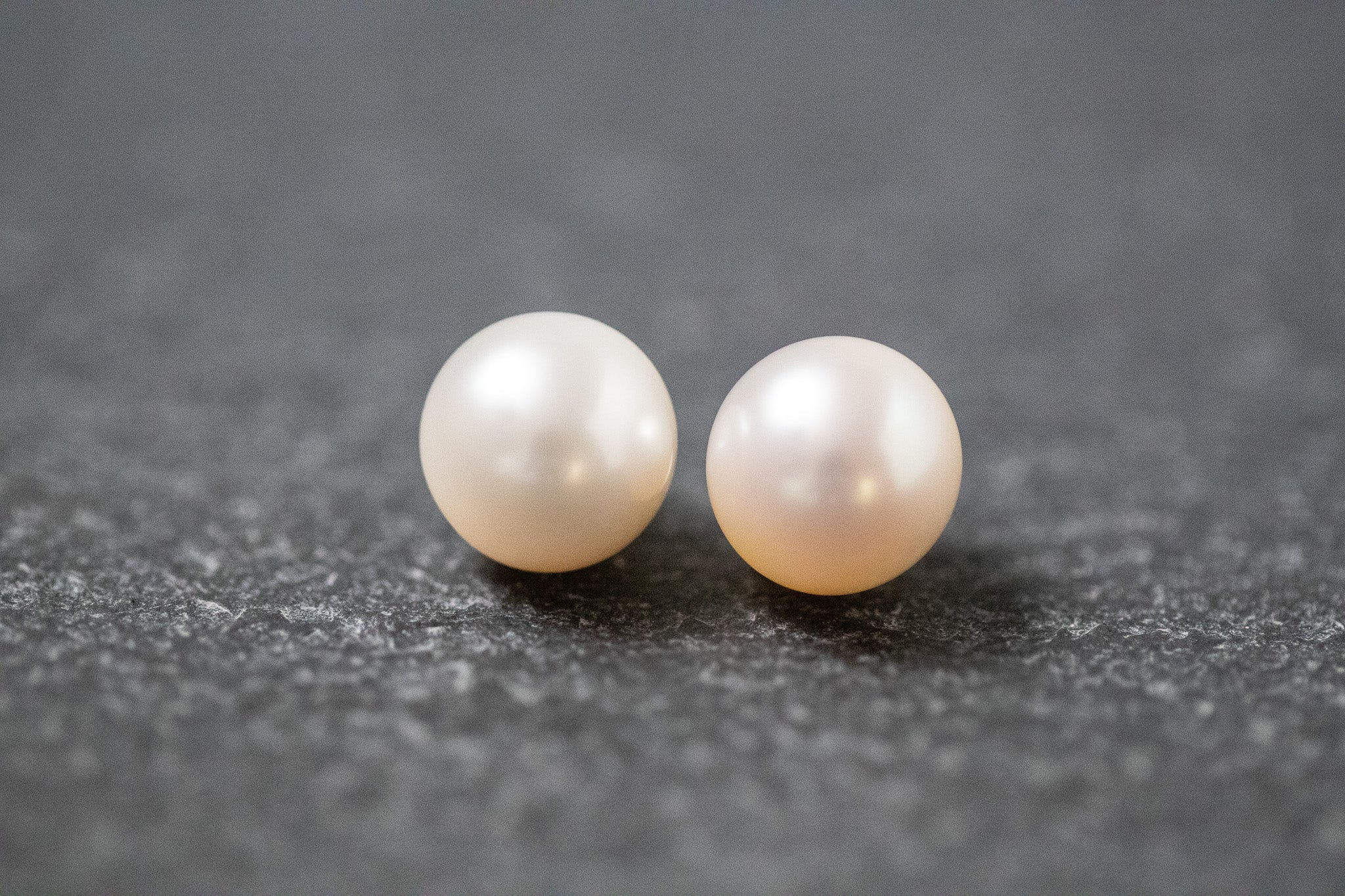 Zwei runde, weiße Frischwasserperlen mit glatter Oberfläche und zartem Glanz, nebeneinander liegend auf neutralem Hintergrund.