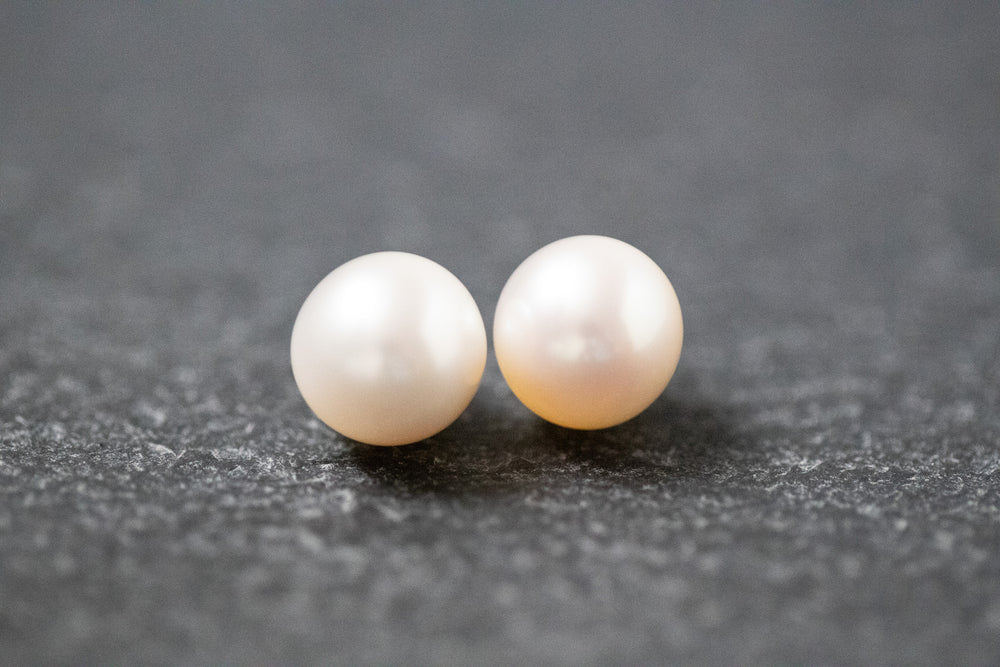 Zwei runde, weiße Frischwasserperlen mit glatter Oberfläche und zartem Glanz, nebeneinander liegend auf neutralem Hintergrund.