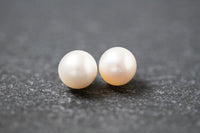 Zwei runde, weiße Frischwasserperlen mit glatter Oberfläche und zartem Glanz, nebeneinander liegend auf neutralem Hintergrund.