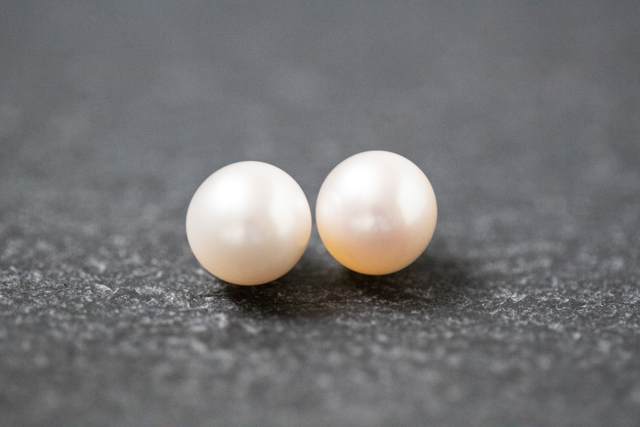 Zwei runde, weiße Frischwasserperlen mit glatter Oberfläche und zartem Glanz, nebeneinander liegend auf neutralem Hintergrund.