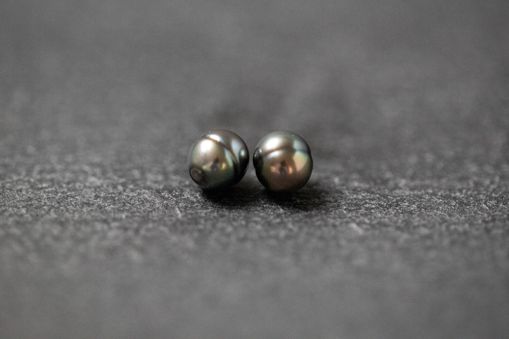 Zwei ovale, gerillte Tahitiperlen in schimmerndem Grau-Grün mit natürlicher Struktur.