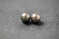 Zwei runde, graue Tahitiperlen mit intensivem Schimmer, nebeneinander auf neutralem Untergrund präsentiert