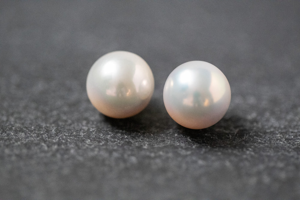 Zwei weiße, runde Frischwasserperlen mit sanftem Glanz, nebeneinander liegend auf neutralem Hintergrund.