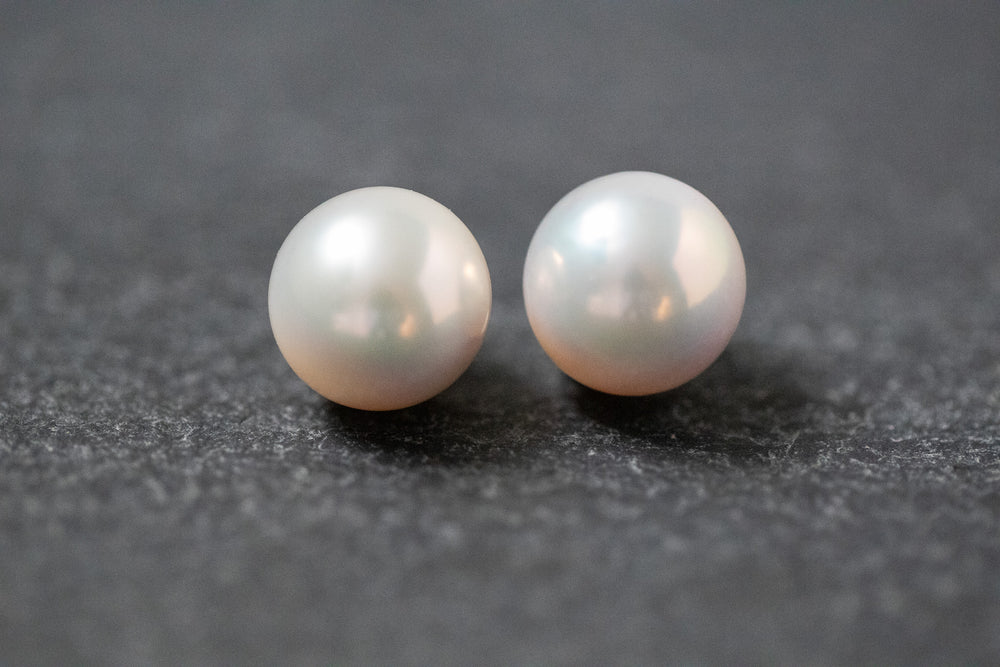 Zwei weiße, runde Frischwasserperlen mit sanftem Glanz, nebeneinander liegend auf neutralem Hintergrund.