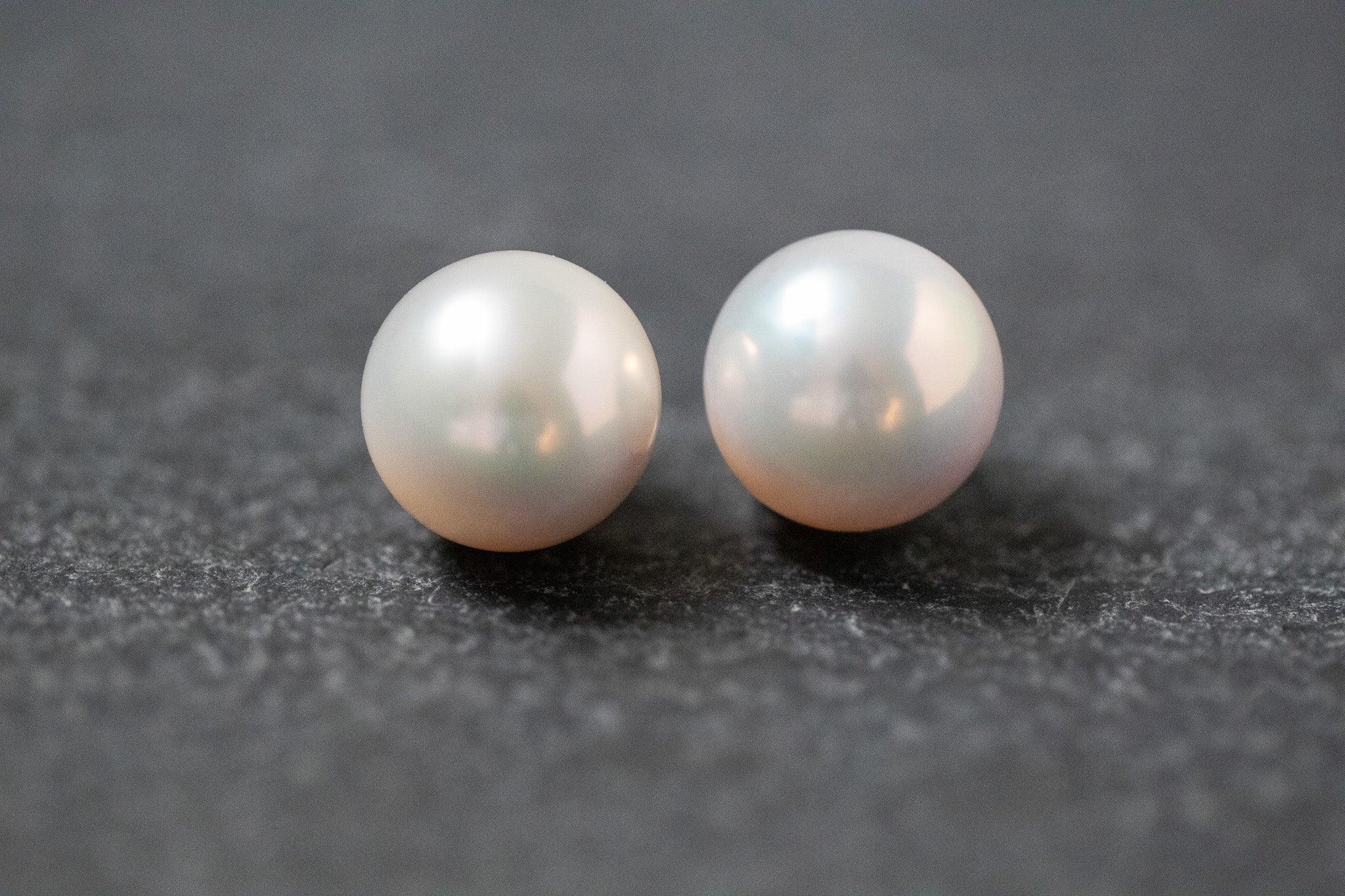 Zwei weiße, runde Frischwasserperlen mit sanftem Glanz, nebeneinander liegend auf neutralem Hintergrund.