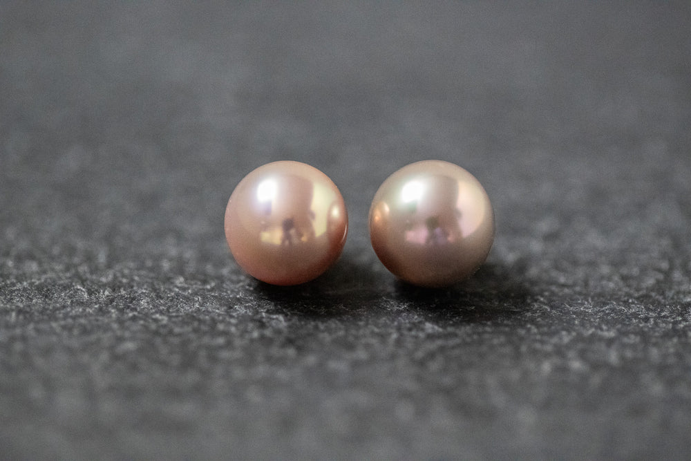 Zwei runde Frischwasserperlen in zartem Rosa mit sanftem Glanz, nebeneinander auf neutralem Hintergrund.