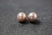 Zwei runde Frischwasserperlen in zartem Rosa mit sanftem Glanz, nebeneinander auf neutralem Hintergrund.