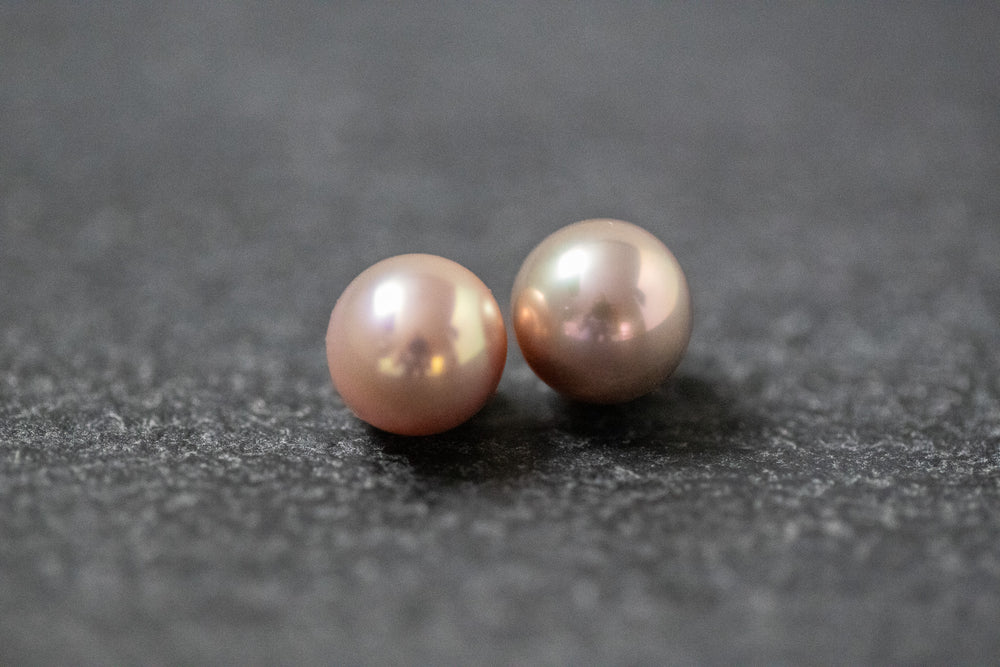 Zwei runde Frischwasserperlen in zartem Rosa mit sanftem Glanz, nebeneinander auf neutralem Hintergrund.