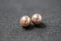 Zwei runde Frischwasserperlen in zartem Rosa mit sanftem Glanz, nebeneinander auf neutralem Hintergrund.
