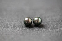 Zwei runde, dunkle Tahitiperlen mit starkem, metallischem Glanz auf dunklem Untergrund nebeneinander platziert