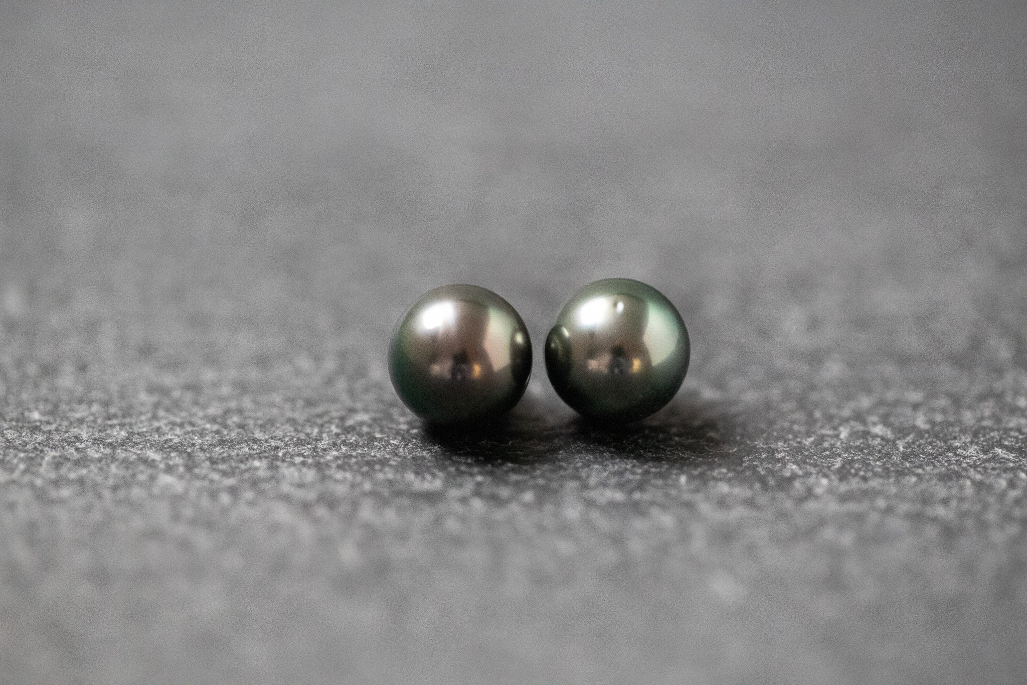 Zwei runde, dunkle Tahitiperlen mit starkem, metallischem Glanz auf dunklem Untergrund nebeneinander platziert