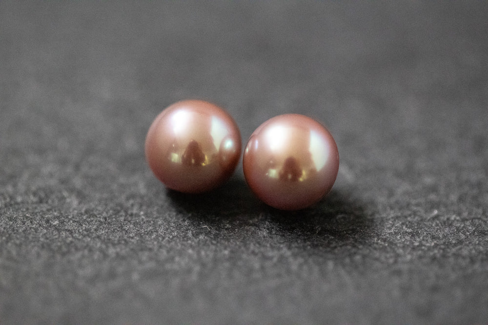 Zwei runde Frischwasserperlen in Dunkelrosa mit zartem Glanz auf hellem Untergrund – ideal für handgefertigten Schmuck.