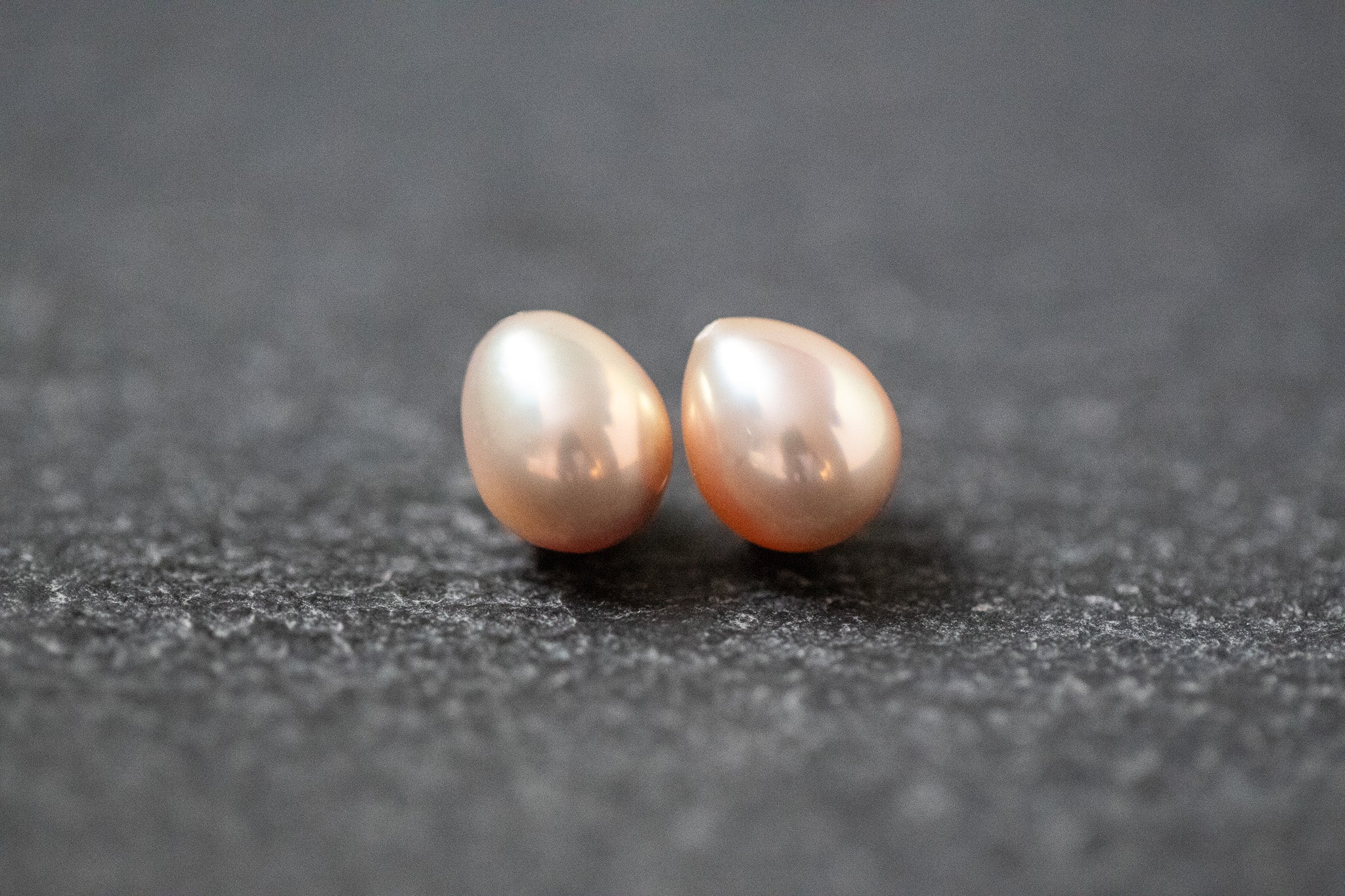 Zwei tropfenförmige Frischwasserperlen in zartem Apricot mit natürlichem Glanz, nebeneinander liegend auf hellem Hintergrund.