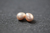 Zwei tropfenförmige Frischwasserperlen in zartem Apricot mit natürlichem Glanz, nebeneinander liegend auf hellem Hintergrund.