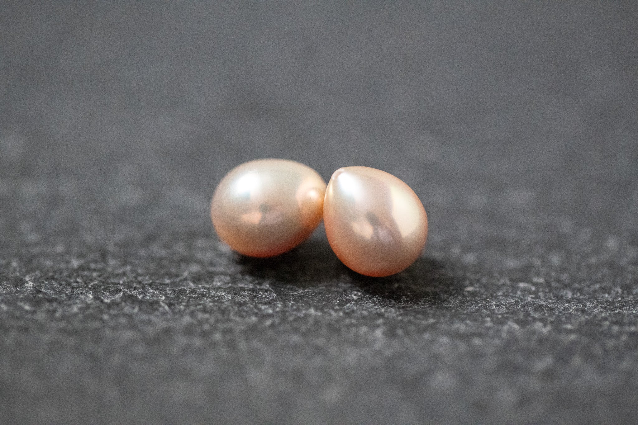 Zwei tropfenförmige Frischwasserperlen in zartem Apricot mit natürlichem Glanz, nebeneinander liegend auf hellem Hintergrund.